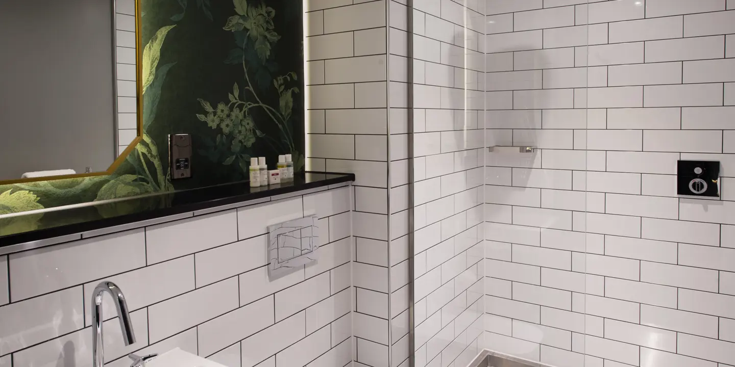 Bathroom featuring a sink, mirror and shower all white tiled.