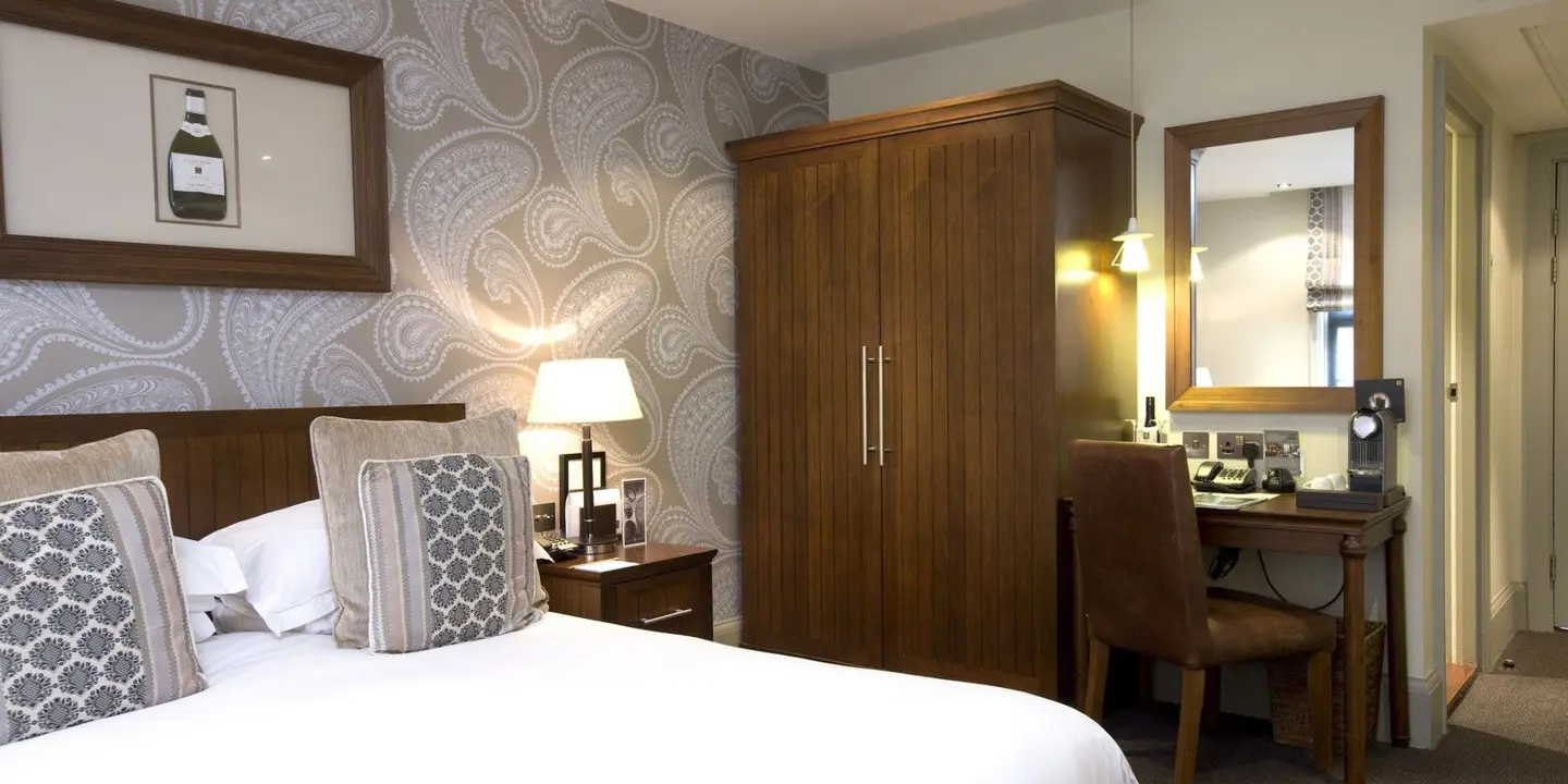 An elegantly furnished hotel room featuring a comfortable bed, a spacious desk, and a stylish mirror.