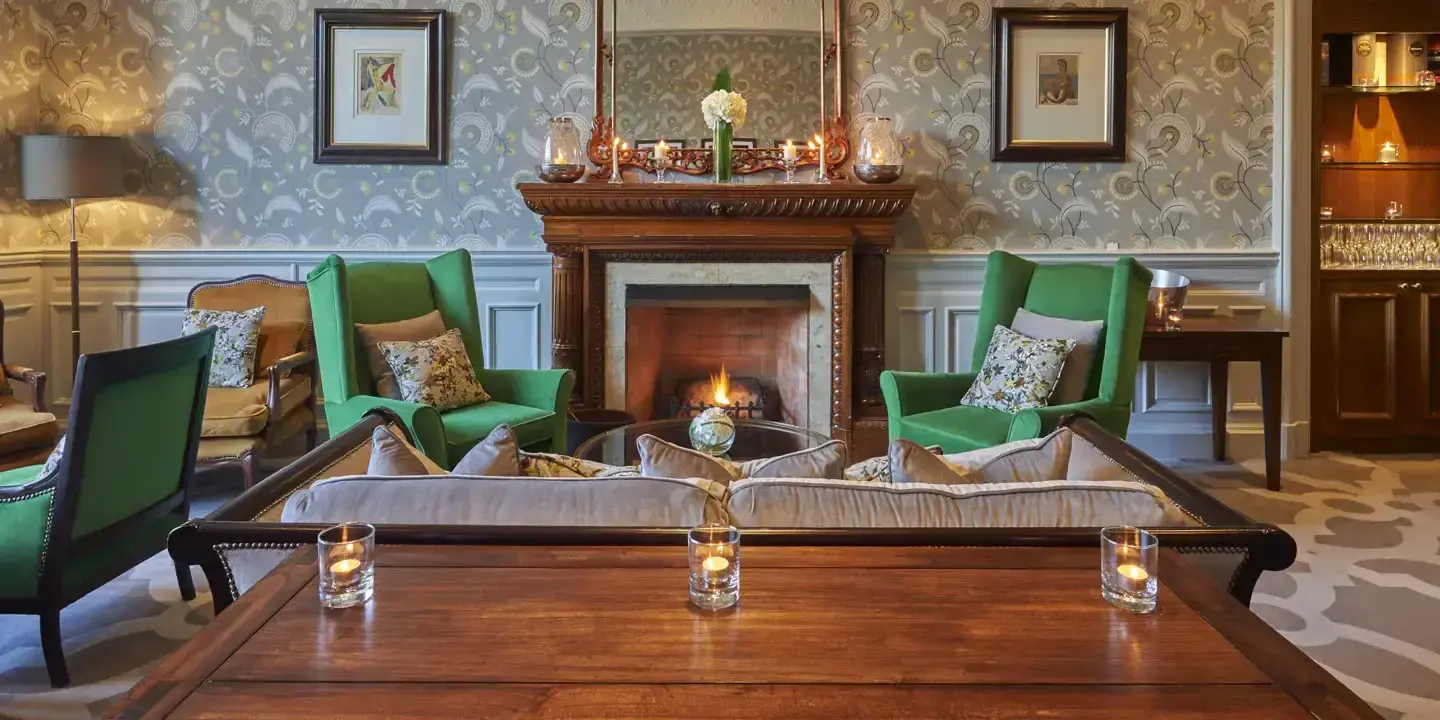 Cosy room with a fireplace in the centre and green arm chairs surrounding