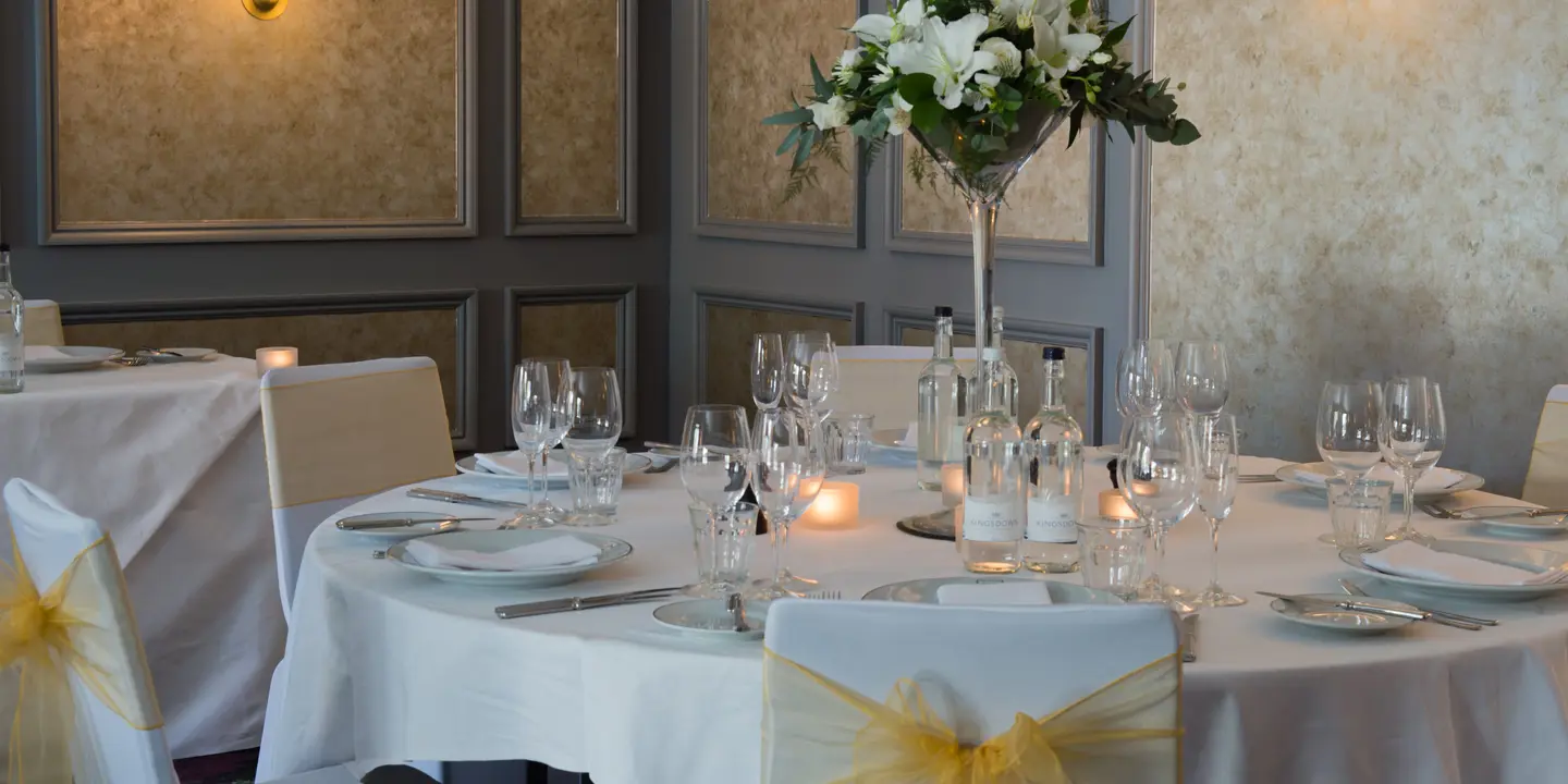 A table elegantly arranged for a formal dinner adorned with white and yellow decorations.