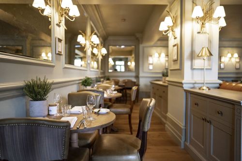 Elegant Bistro du Vin dining room with neatly set wooden tables, upholstered chairs, decorative mirrors and warm wall lighting.