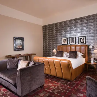 A suite decorated with red carpet and neutral colour furniture. There is a brown leather bed and grey fabric sofas