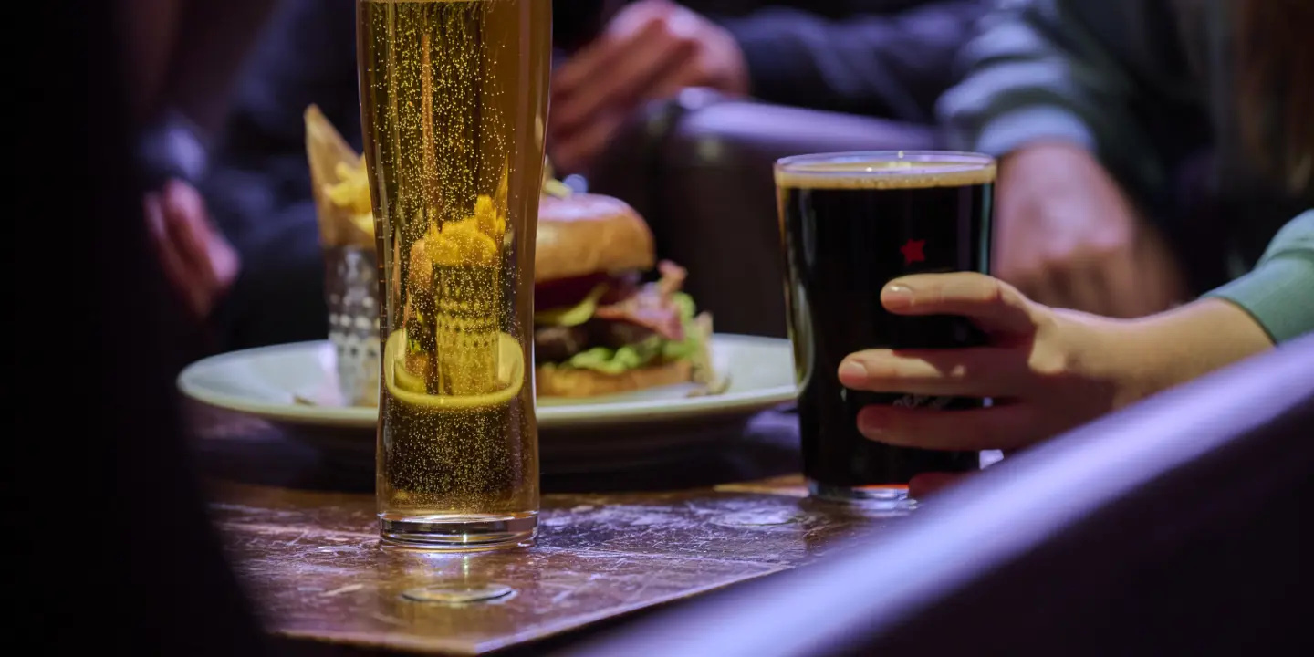 People around a table enjoying beers, with a plate of burger and chips on the table