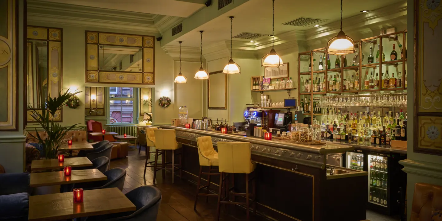 A bar with seating across the main bar and tables, the tables are candle lit and there is a range of drinks behind the bar.