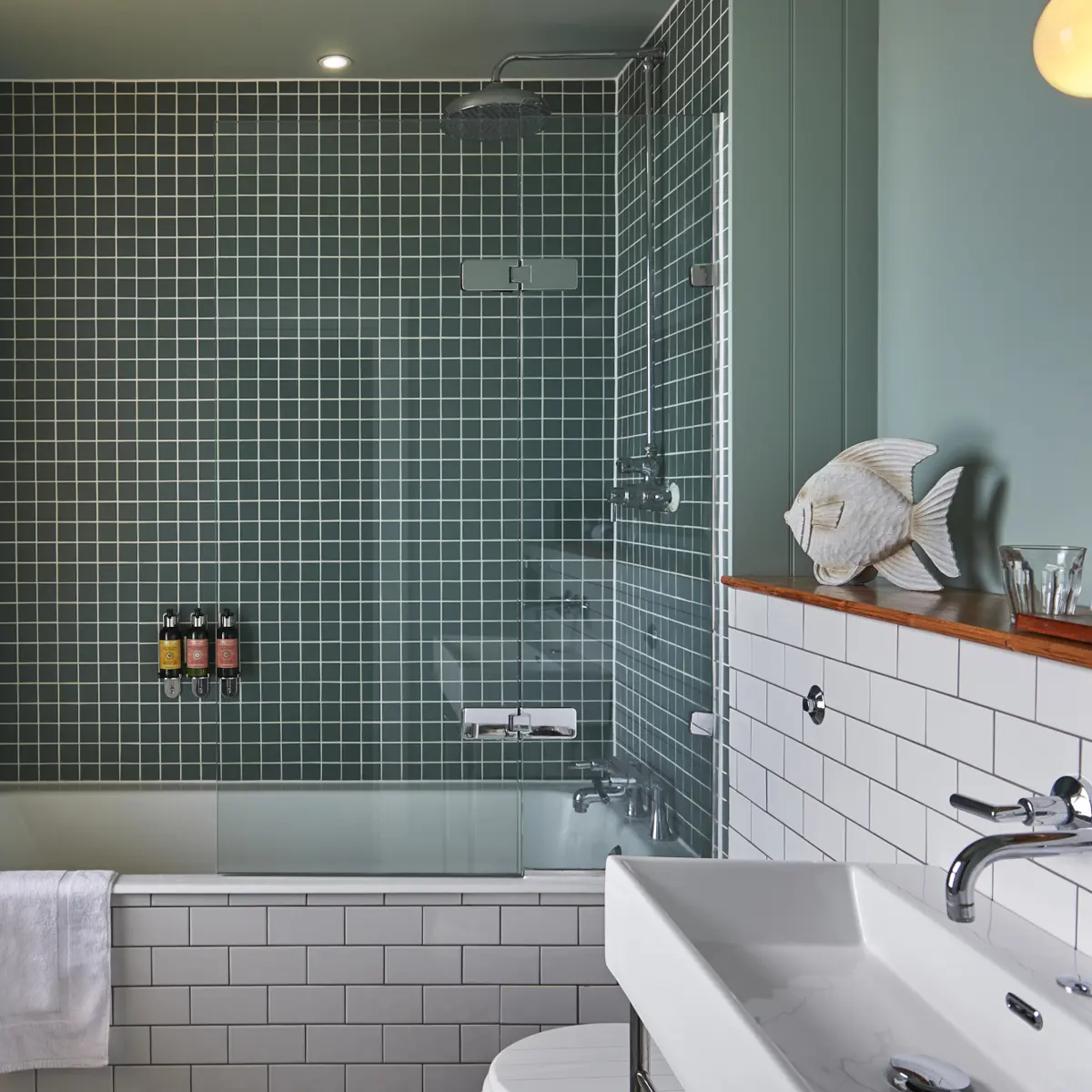 Bathroom featuring a bathtub, sink, and toilet and green tiles.