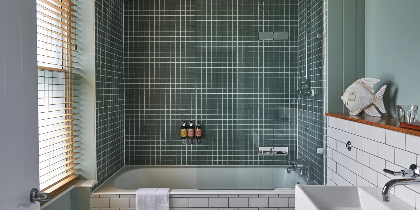 Bathroom featuring a bathtub, sink, and toilet and green tiles.