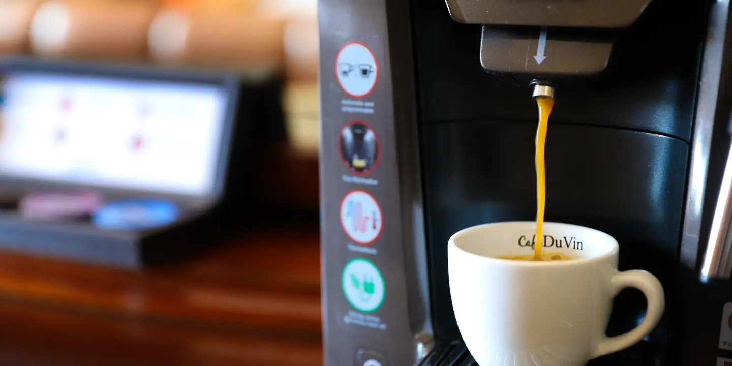 A cup of coffee being poured by a coffee machine