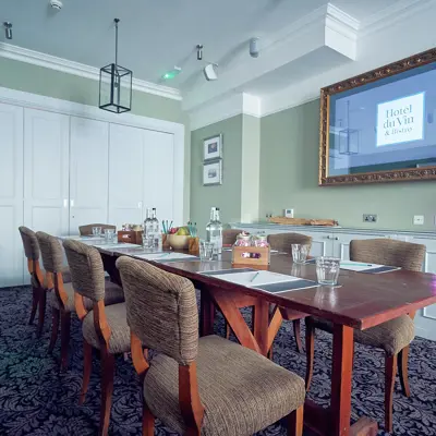 Conference room featuring a spacious wall-mounted screen, long table surrounded with chairs.