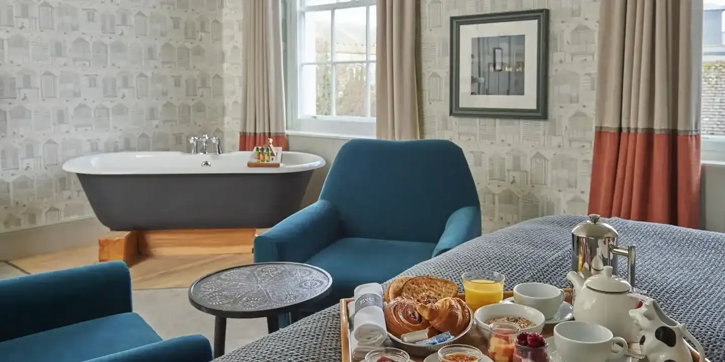 Breakfast tray placed on a bed with a bathtub in the background.