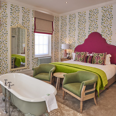 Bedroom featuring a comfortable bed, green armchairs and bathtub.