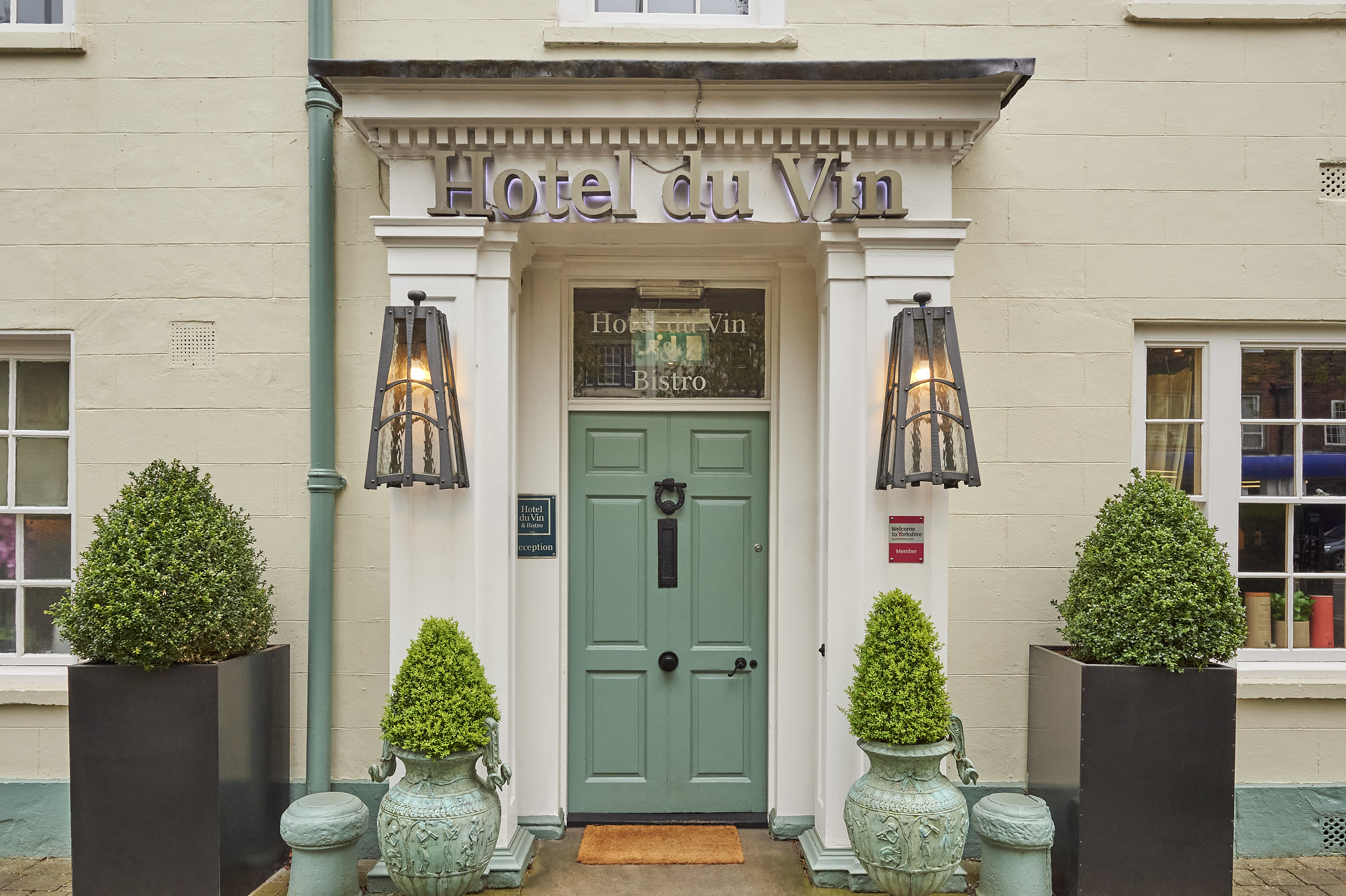 Entrance to a hotel featuring green door and four large planters