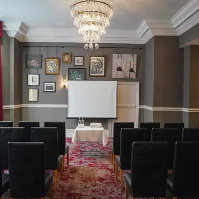 An image depicting a well-furnished room with chairs and a projector screen.