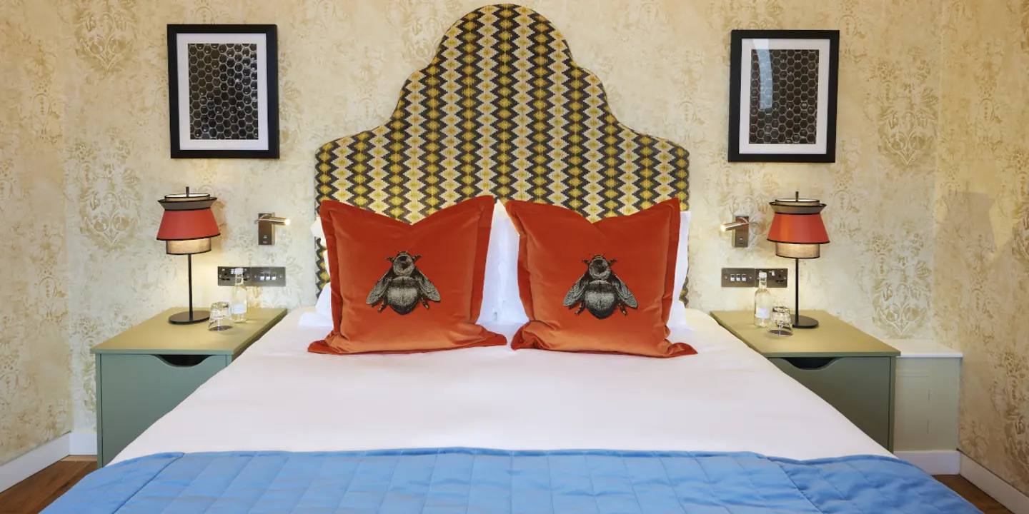 A neatly made bed adorned with two pillows with bees printed on them.