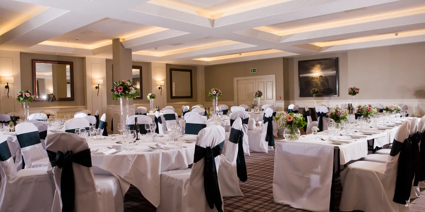 A banquet room adorned with elegantly draped white linens, featuring tables and chairs neatly arranged for a sophisticated gathering.