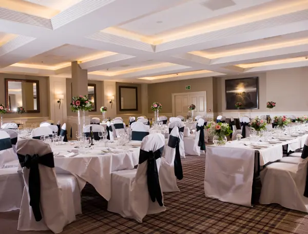 A banquet room adorned with elegantly draped white linens, featuring tables and chairs neatly arranged for a sophisticated gathering.