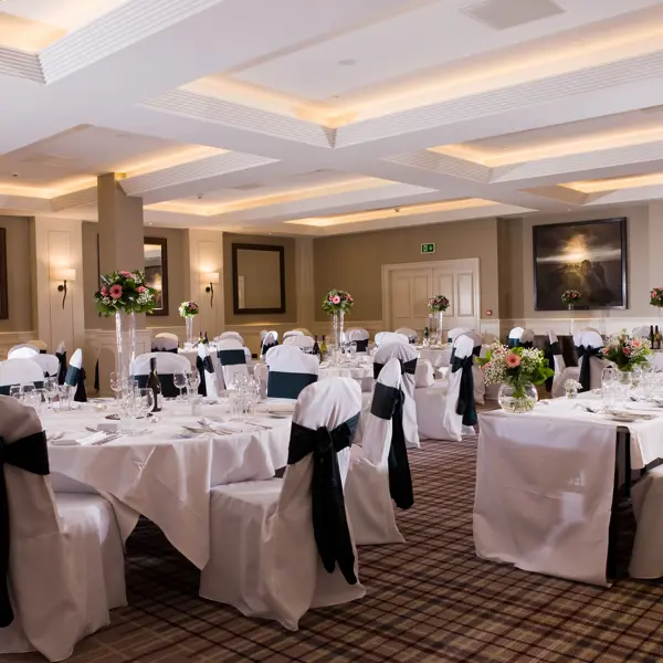 A banquet room adorned with elegantly draped white linens, featuring tables and chairs neatly arranged for a sophisticated gathering.