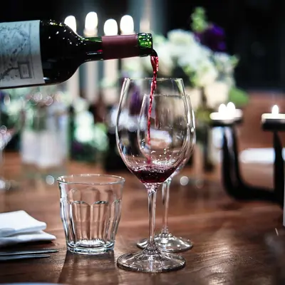 Red wine being poured into a wine glass, which is on a wooden candle-lit table