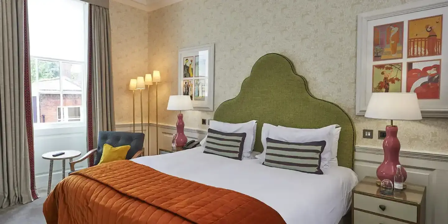 An elegantly furnished hotel room featuring a comfortable bed, green headboard and a stylish chair.