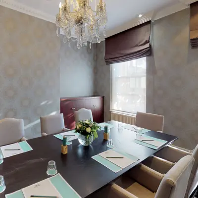 A dining room featuring a long table, chairs, and an elegant chandelier.