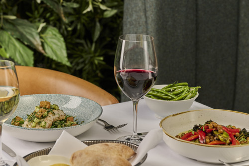 Glass of red wine served alongside seasonal restaurant dishes, including roasted vegetables, green beans and freshly baked bread.