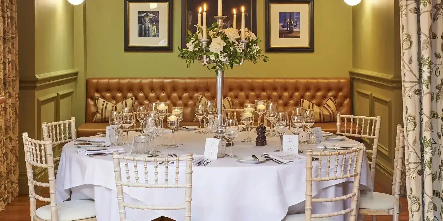 Dining room featuring a spacious banquet table with a white table cloth, surrounded by elegant chairs.
