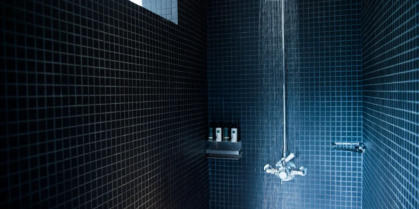 Shower head in a bathroom with blue tiles.