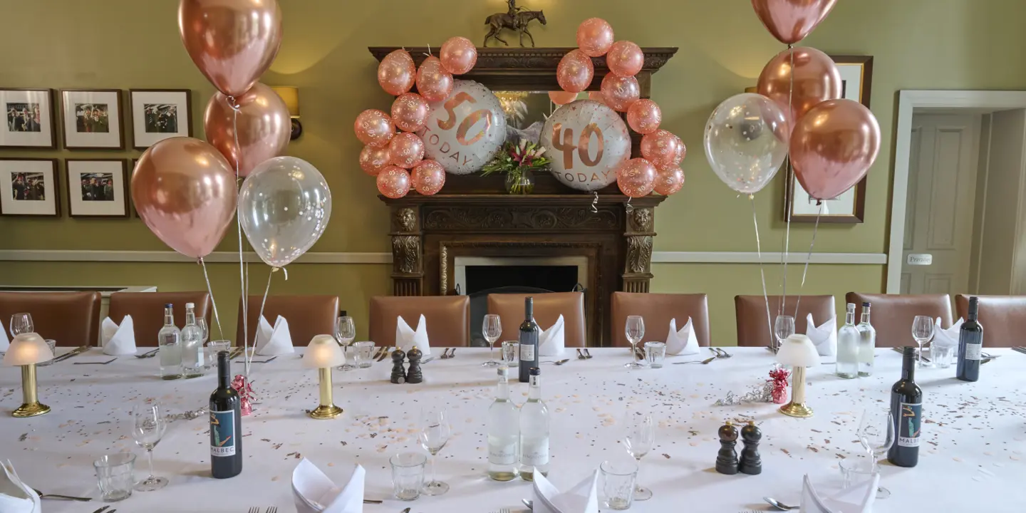 A long table decorated with confetti. There are pink and white balloons across the table