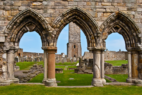 This image shows the historic stone arches and ruins of St Andrews Cathedral, with a tower visible through the central arch.