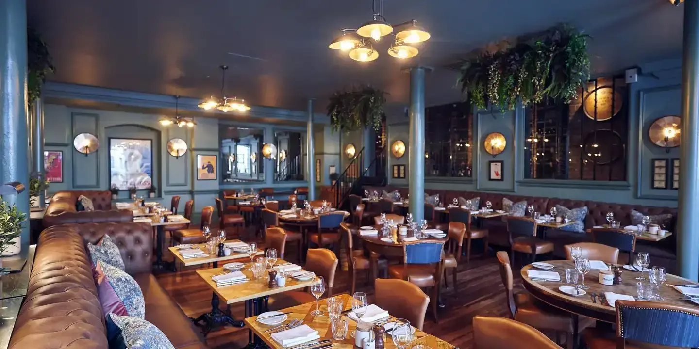 A restaurant featuring numerous tables and chairs with plants hanging from ceiling