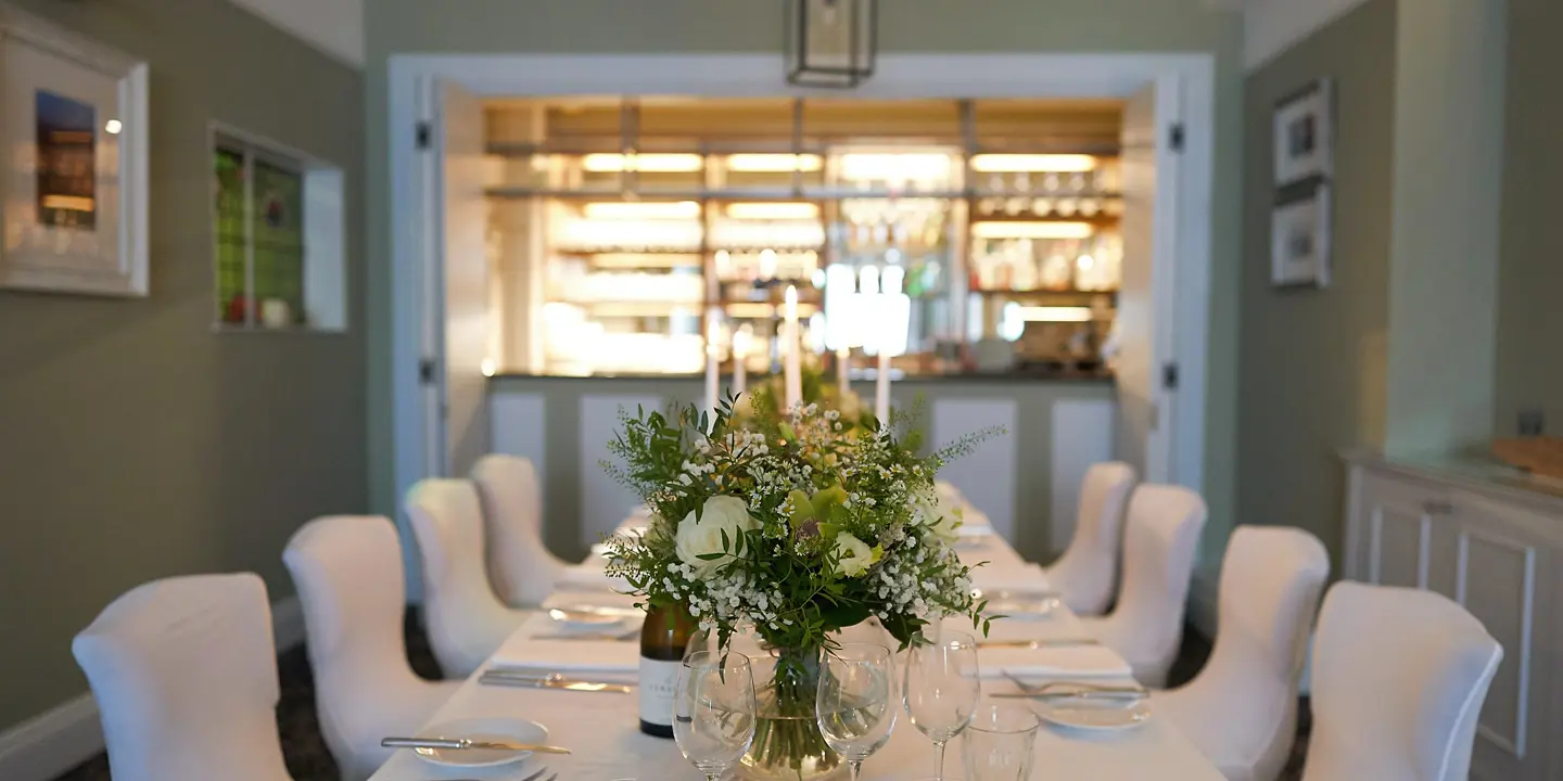 A long table adorned with elegant white chairs and a tastefully arranged vase of flowers.