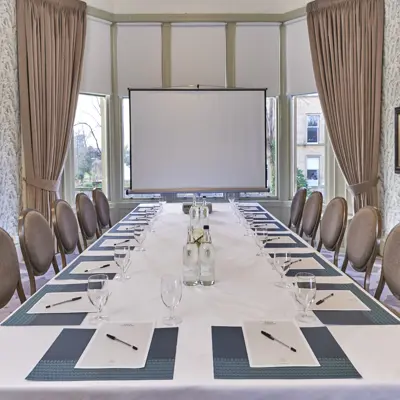 A projector at the far end of the rectangular table that is central and chairs that line each side of the table