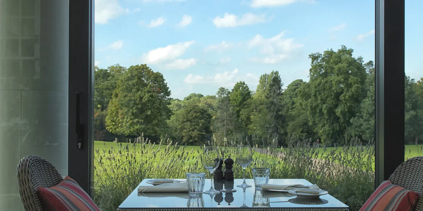 A table featuring two chairs and a bottle of wine placed on top with views of greenery.