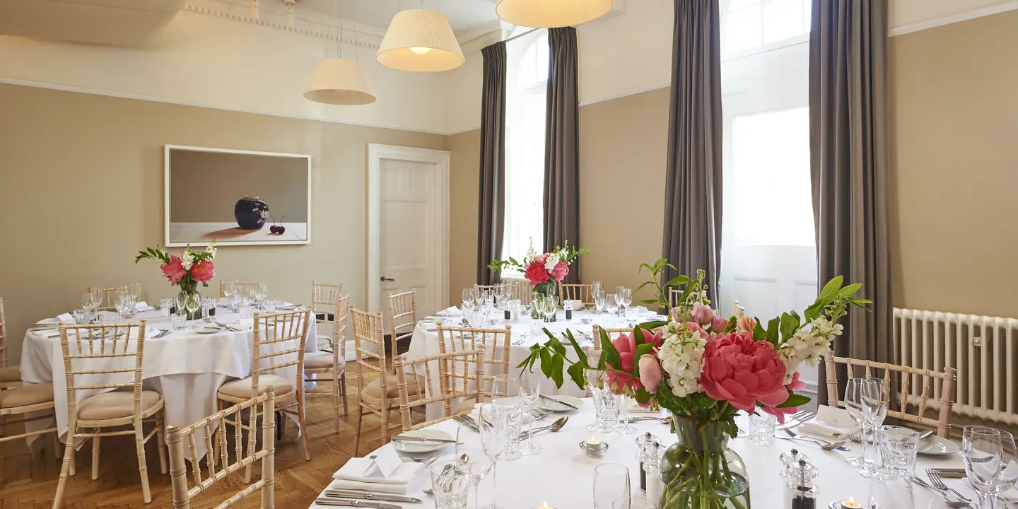 Multiple tables arranged for a formal dinner with a vase of flowers.