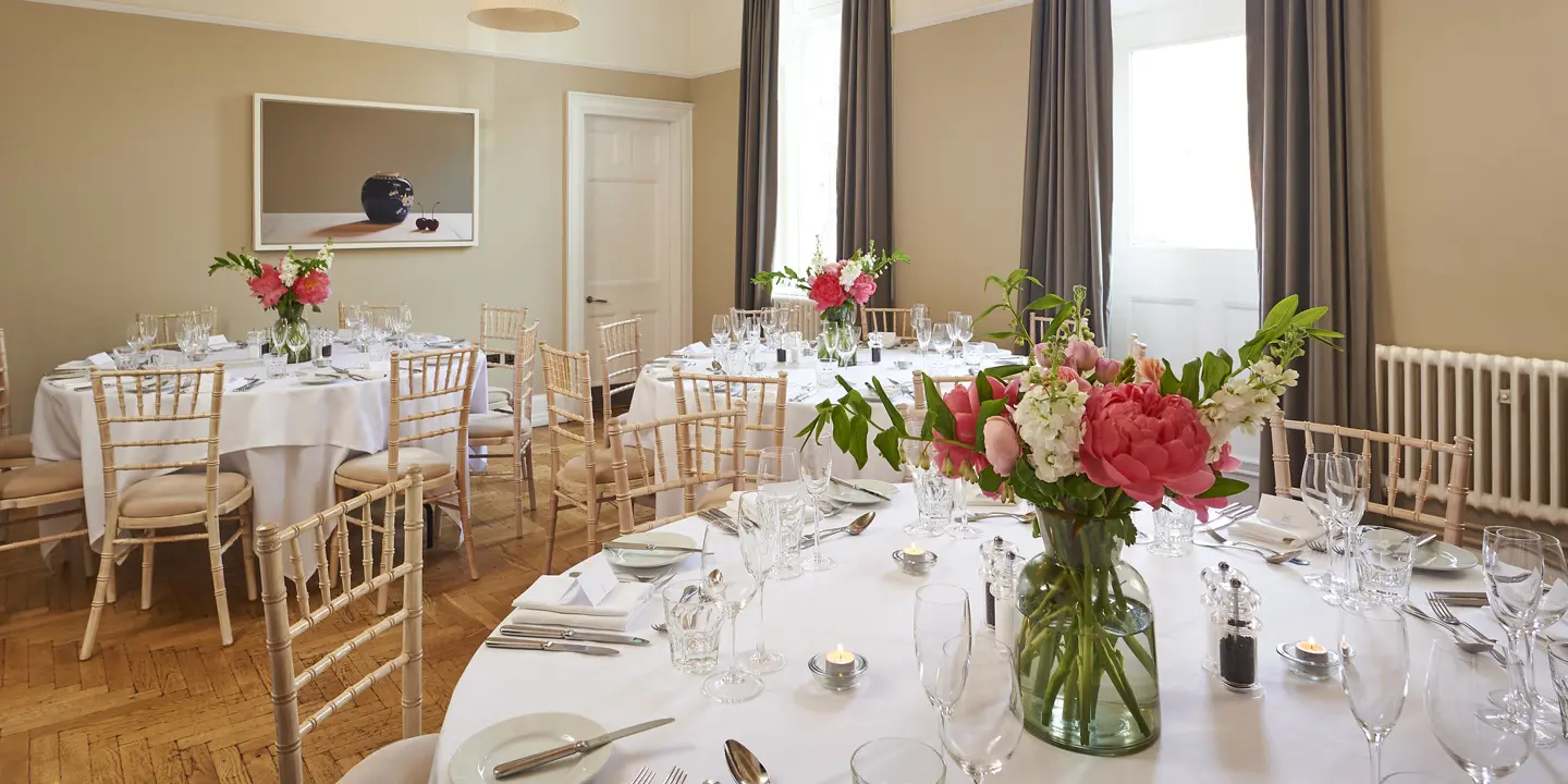 Multiple tables arranged for a formal dinner with a vase of flowers.