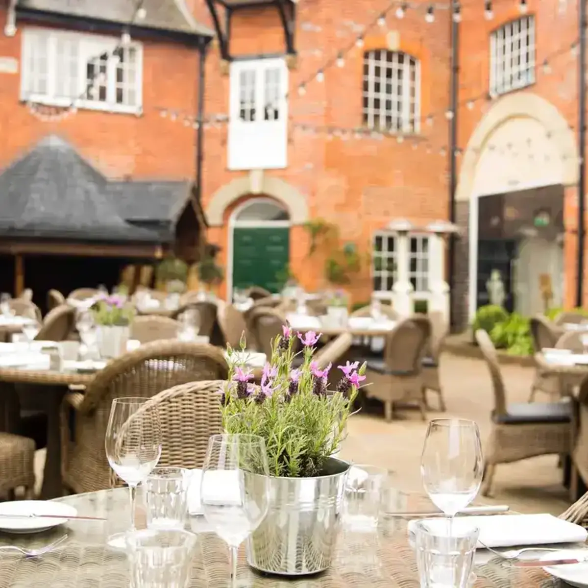 Outdoor dining area with tables dressed with a purple plant and chairs surrounding