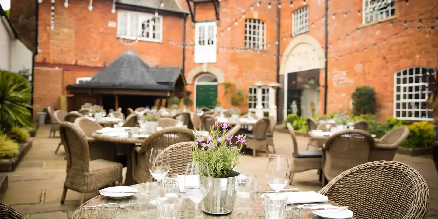 Outdoor dining area with tables dressed with a purple plant and chairs surrounding