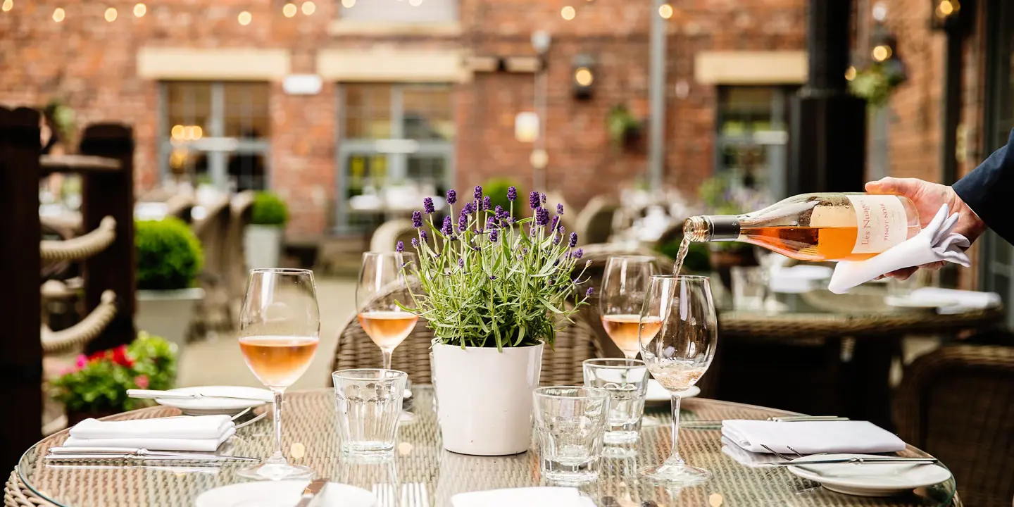 A person pouring wine into a glass on a table.