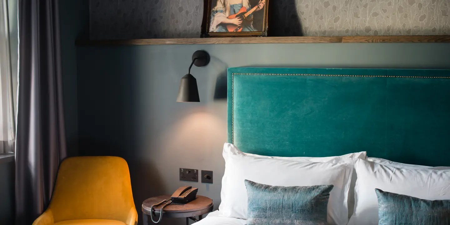 A bed featuring a green headboard and accompanied by a yellow chair.
