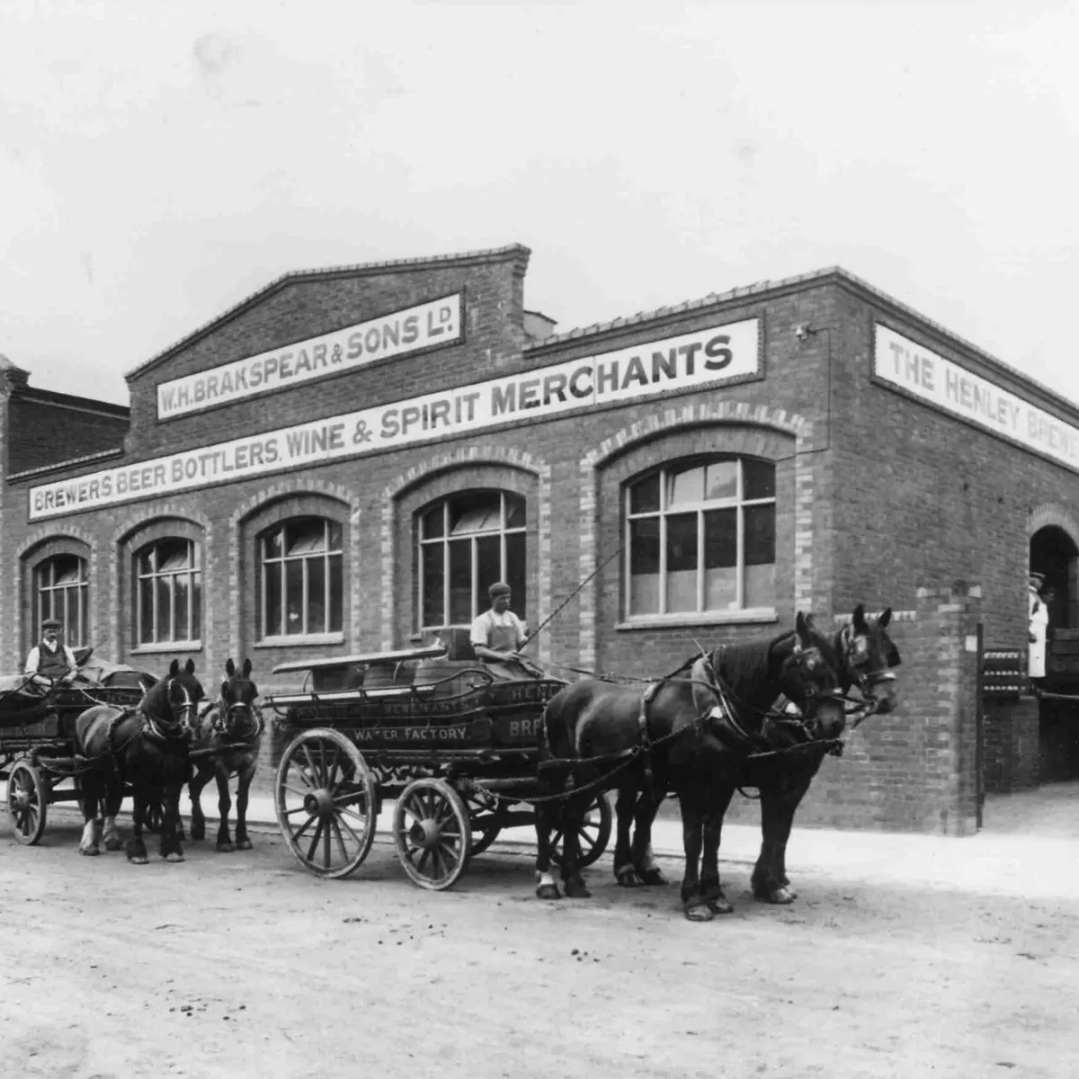 Historic black‑and‑white image of the building that is now Hotel du Vin Henley-on-Thames, originally the Brakspear Brewery, with three horse-drawn carriages parked in front of the brick façade.