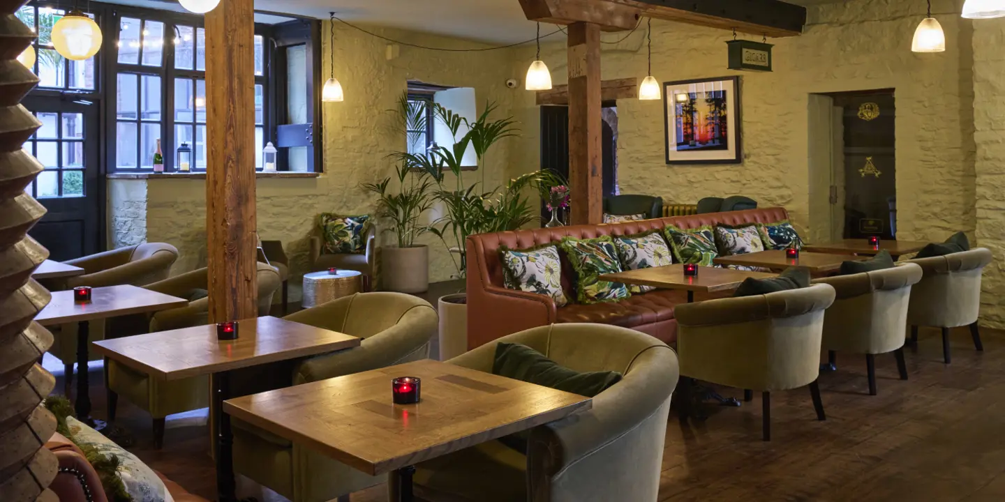 A bar space with leather sofa and fabric chairs, there is a candle in the middle of each table