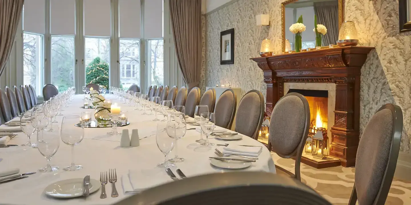 Decorated long white table with glasses ands candles with a cosy fireplace