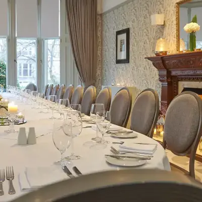 Decorated long white table with glasses ands candles with a cosy fireplace