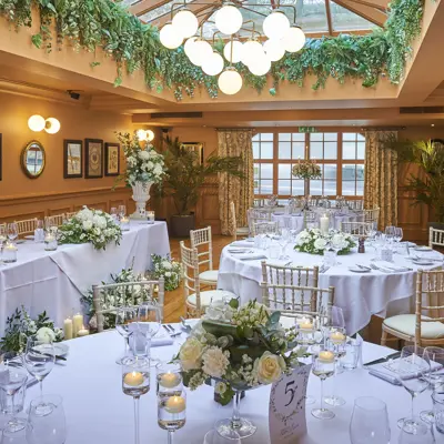A well-lit room furnished with tables, chairs, foliage, and a skylight.