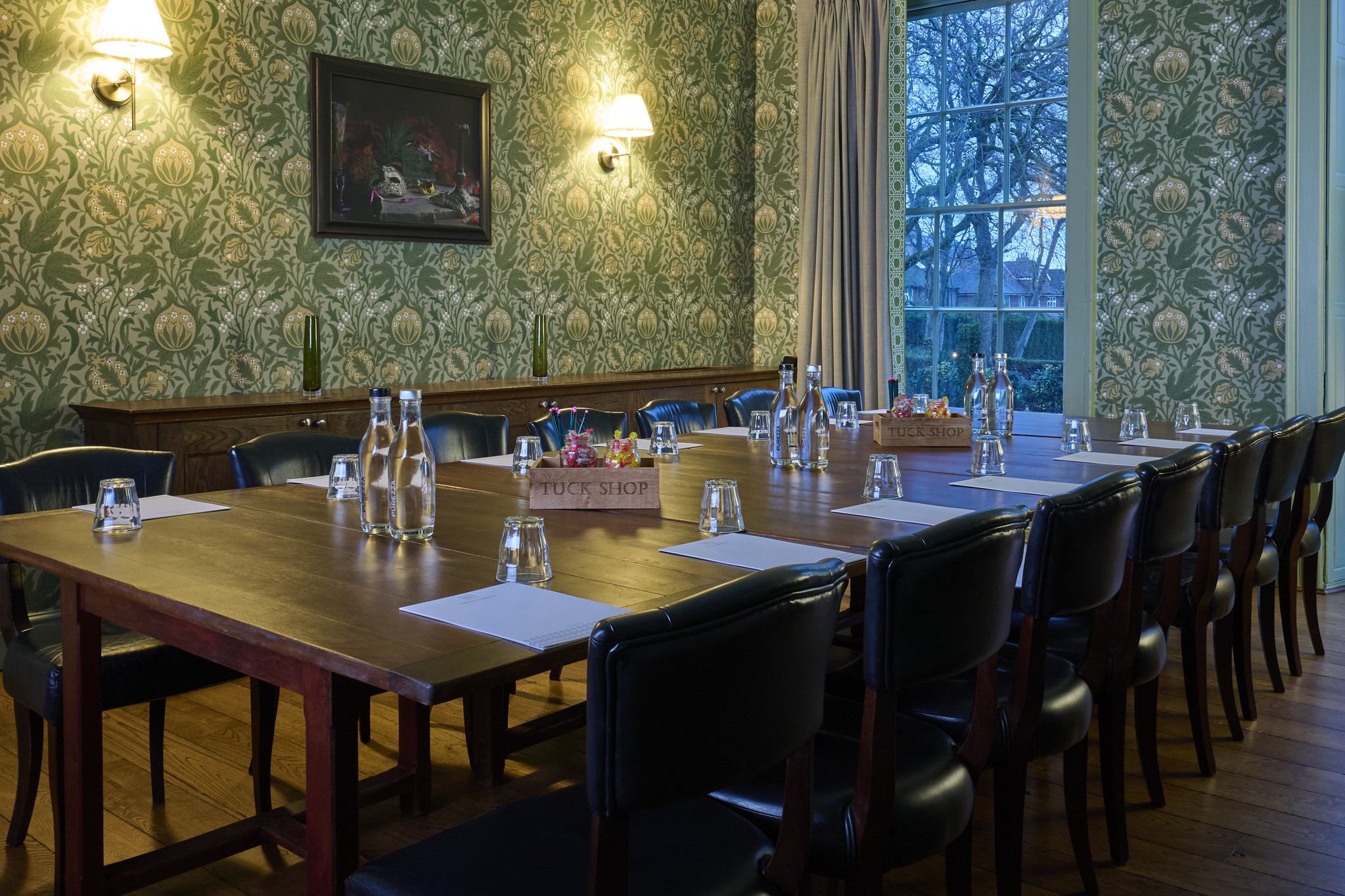 Dining room featuring a prominent wall painting and long wooden table adorned with leather chairs.