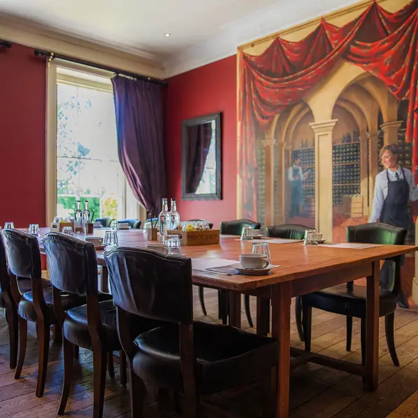 Dining room featuring a prominent wall painting and long wooden table adorned with leather chairs.