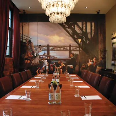 A wooden table adorned with glasses with a large painting of Newcastle's shipyard