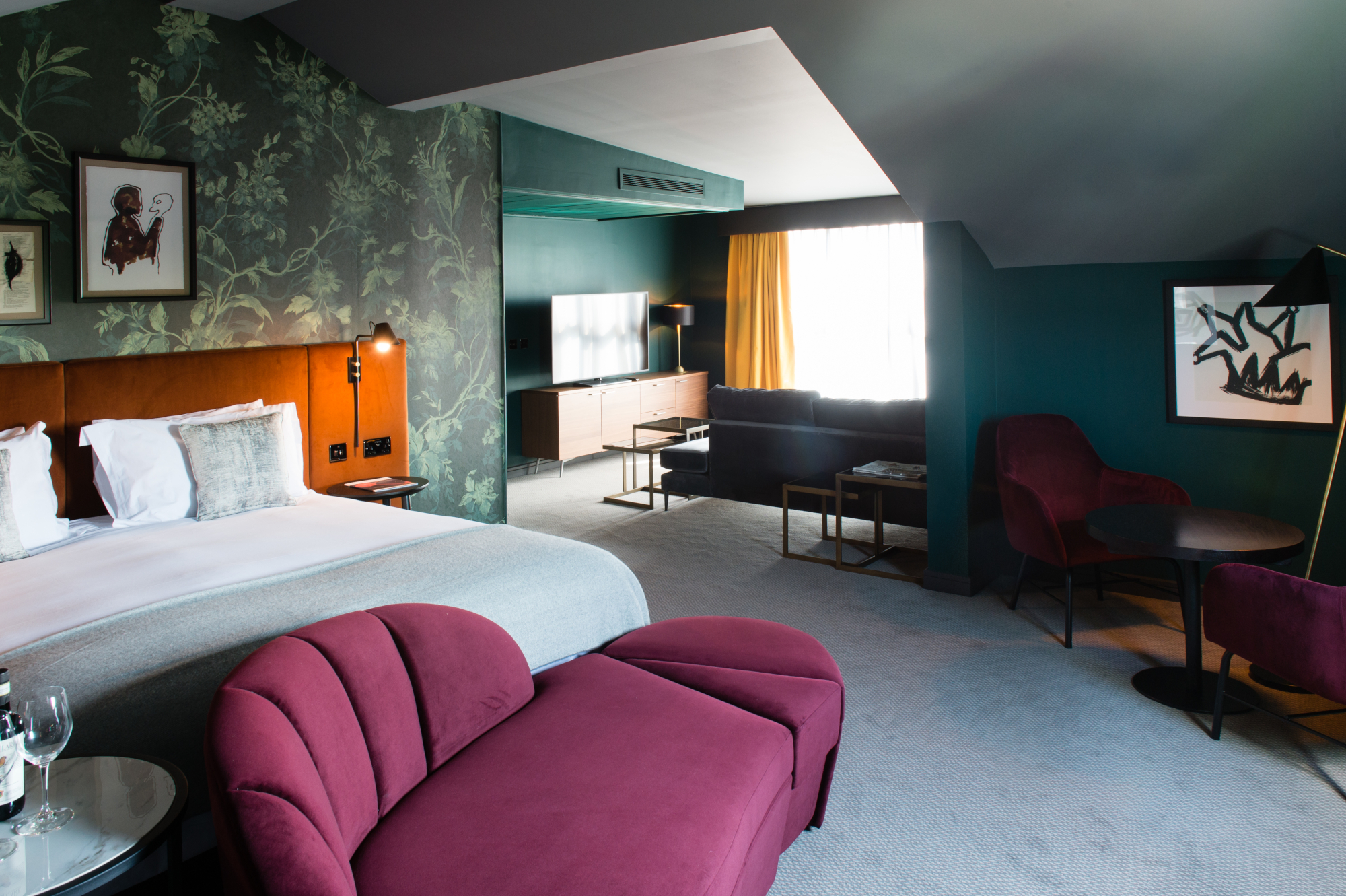 A well-furnished hotel room featuring a comfortable bed, sofa, armchair, and television.