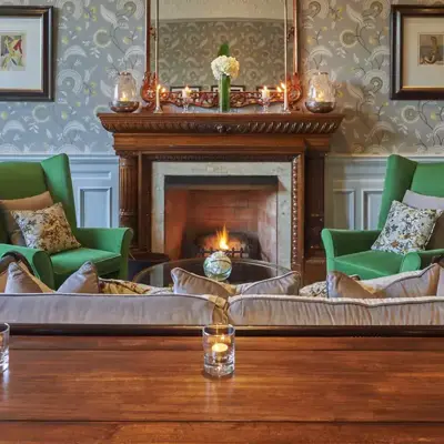 Cosy room with a fireplace in the centre and green arm chairs surrounding