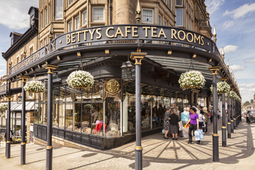 Bettys Café Tea Rooms in Harrogate, featuring its historic corner façade, hanging flower baskets and visitors outside on a sunny day.