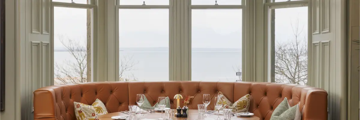 A beautifully arranged table with elegant wine glasses and neatly set place settings, placed in front of a picturesque bay window.